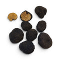 Seven black truffles, including two halves showing their golden-brown nut interiors, arranged on a plain white background.